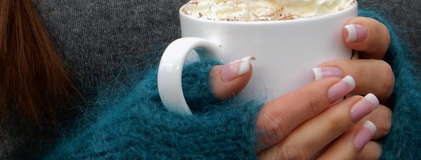 bone china mug with cream and held in hands wearing mohair mittens