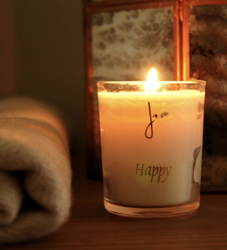 lit candle with happy on front in gold type near cosy lantern and home of juniper blanket